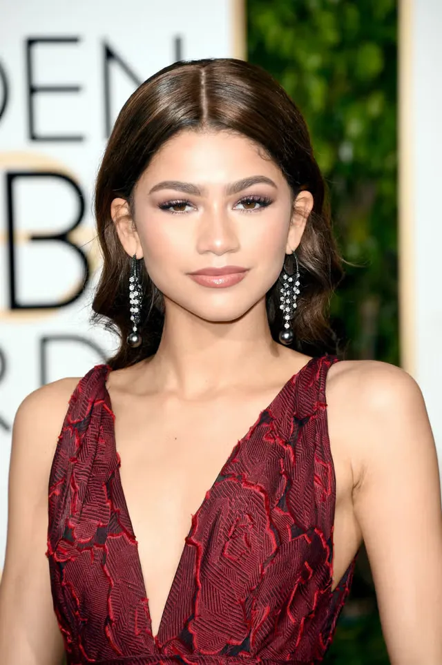 Close-up portrait of Zendaya at the Golden Globes in a deep wine-red embroidered gown, dark wavy hair swept to one side, long cascade diamond earrings.