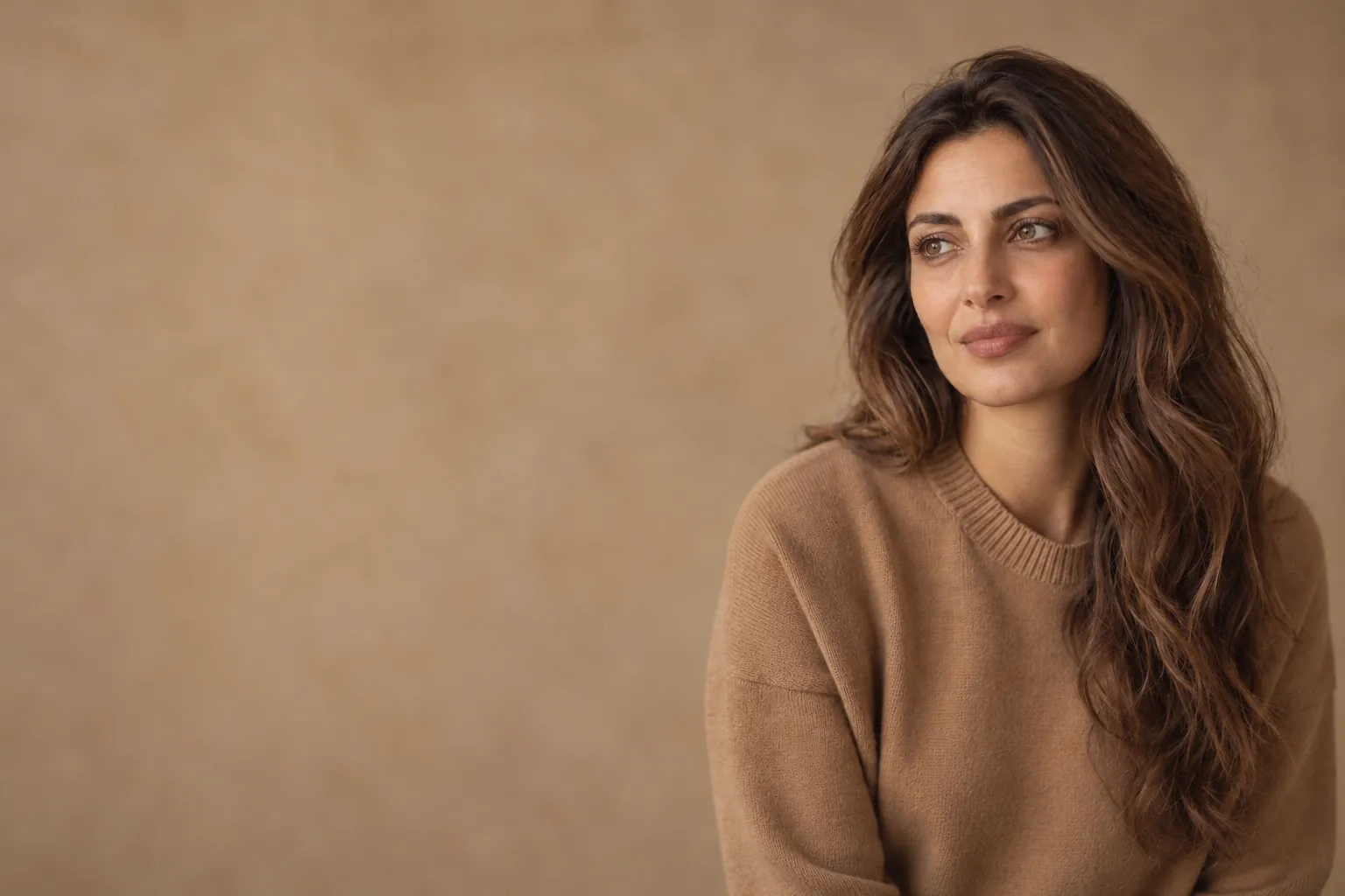 Woman with long warm brown hair and soft hazel eyes in a camel jumper